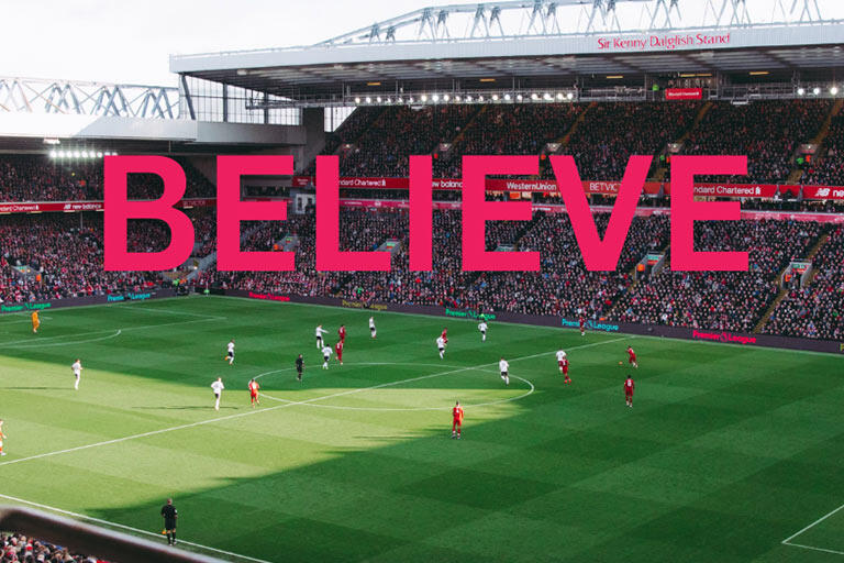 Stadium with an active soccer game and large crowd. The word "BELIEVE" is written on top.