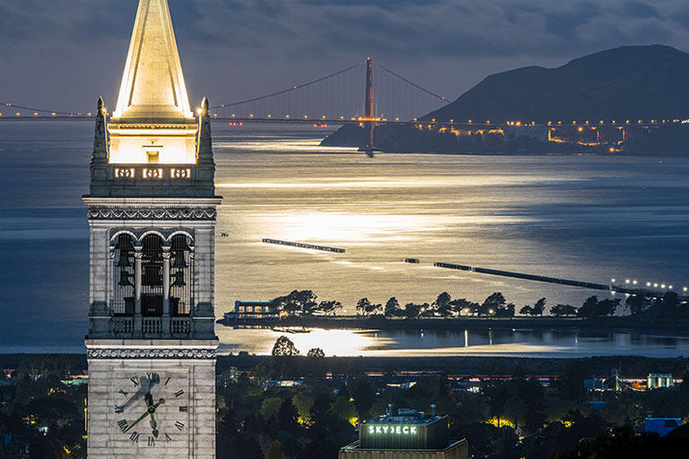 Night shot of UC Berkeley’s Campanile with the Golden Gate Bridge in the background and the bay lit by the moon.