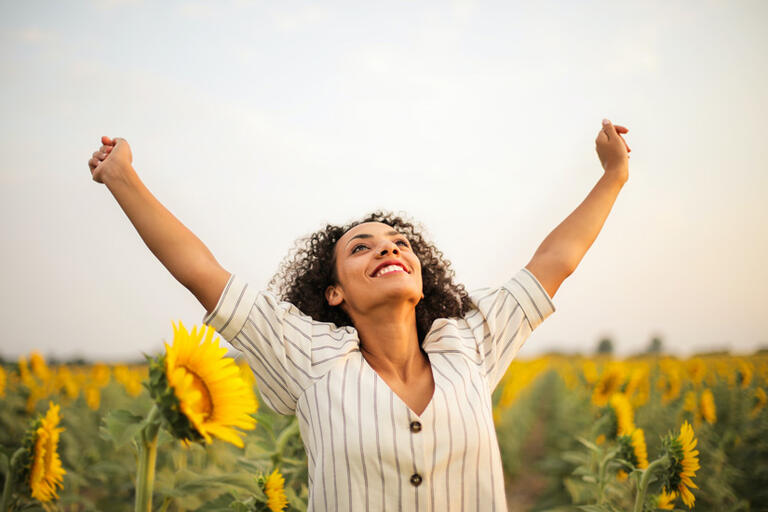 Excited woman stands in a field of sunflowers with her arms up
