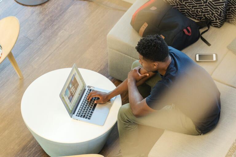 Overhead view of a young person sitting on a couch and working on a laptop