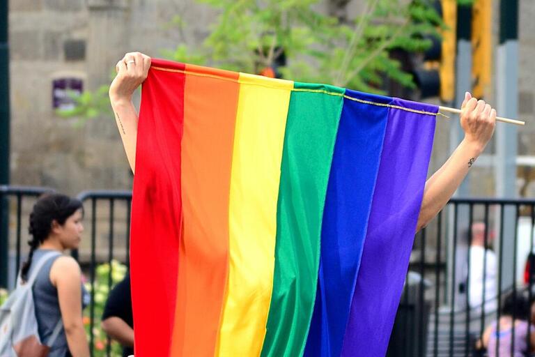 A rainbow pride flag is held up, the person holding it is hidden behind the large flag