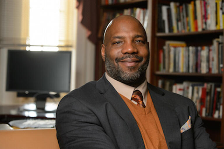 Dr. Jelani Cobb stands in front of a fully stocked bookshelf.