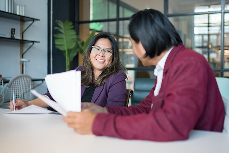 Two employees smile and chat while working through paperwork.