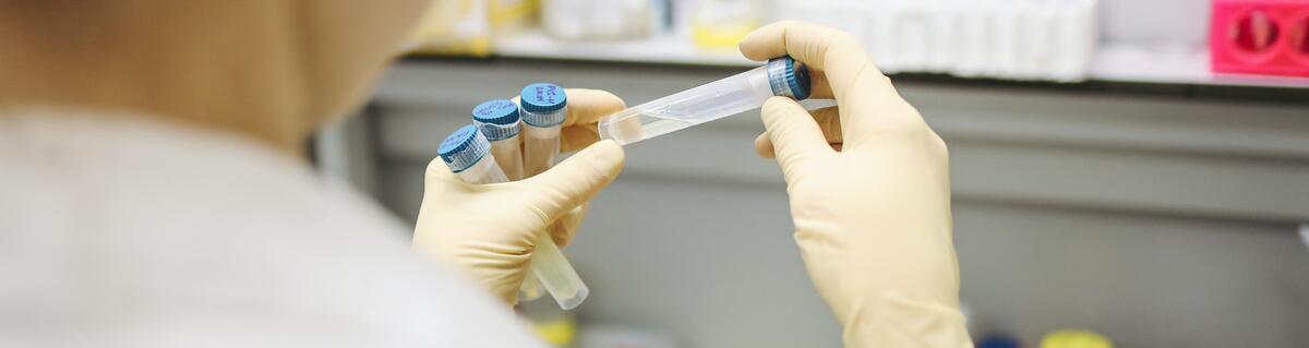 Hands in latex gloves holding four plastic vials above a desk