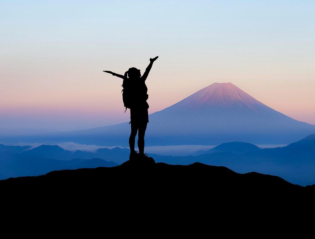 Silhouette of a person with their arms in the air standing on top of a mountain
