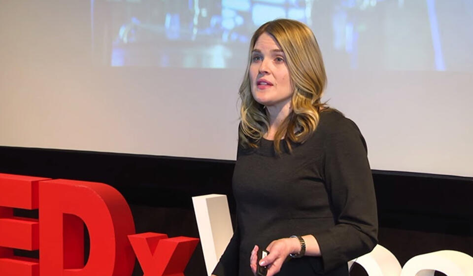 A woman in a black dress giving her Tedx presentation.