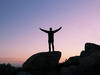 Silhouette of a person with their arms in the air standing on top of a rock with a sunset in the background